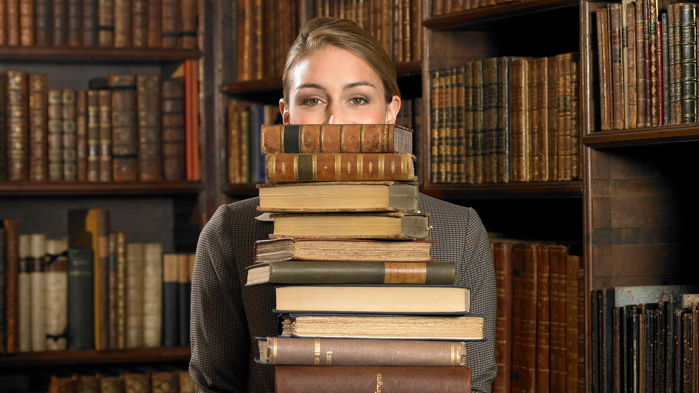 Woman holds a stack of old books in a library