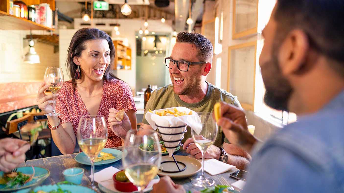 A close-up of female and male friends sitting in a bar in Perth, Australia, having a meal and drink together. The main focus is on a man and woman part of the group.